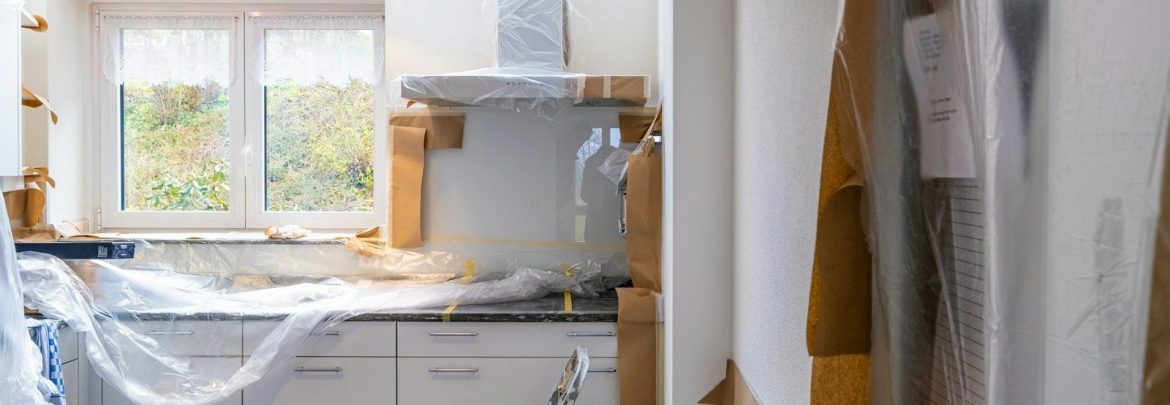 A kitchen under renovation with white cabinets covered in plastic and brown paper